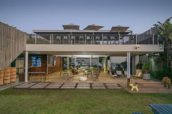 The beach clubhouse at dusk, its lights on above the lawn