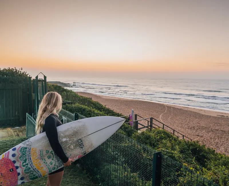 A resident carrying a surfboard down the path to the beach