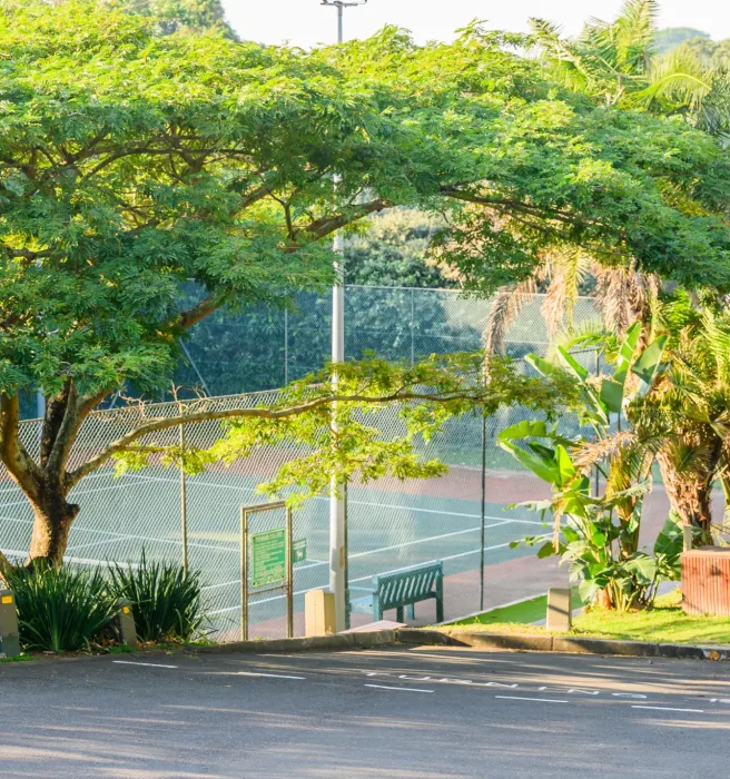A floodlit tennis court behind the trees at the edge of the estate